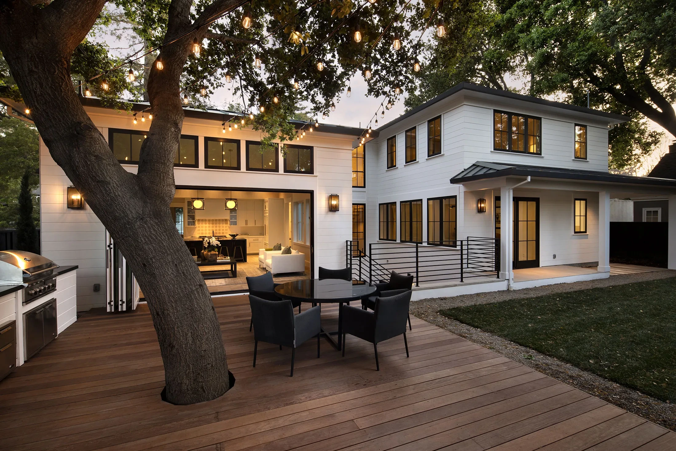 Covered outdoor living area and deck at dusk beneath an oak on a GHG Builders custom home